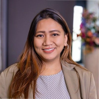 Joanne Guevarra Neelis, lachend, in een beige blazer tegen een zacht verlicht interieur